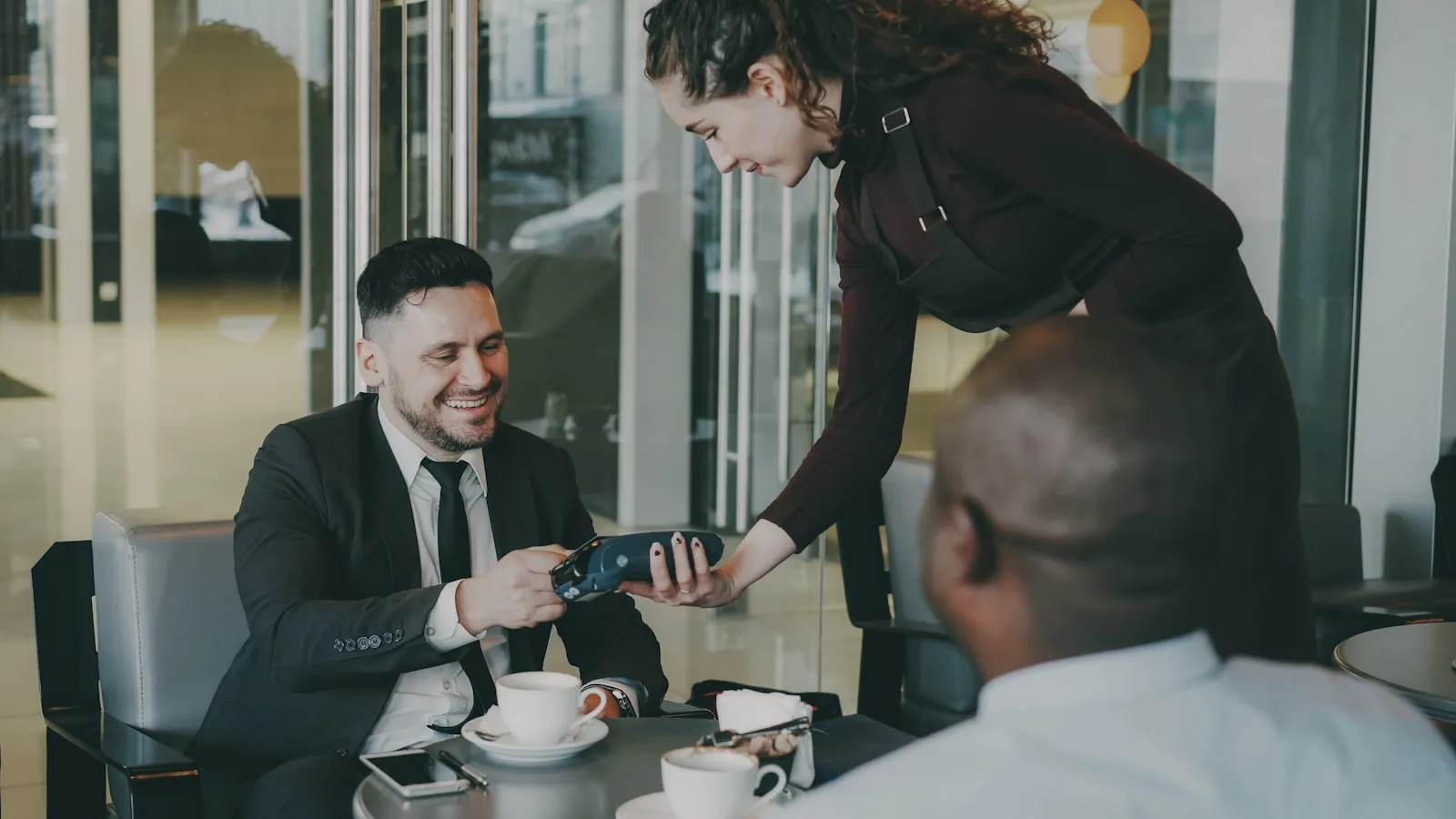 Un serveur tend un terminal de paiement à un client au restaurant, illustration du pourboire ajouté à la note